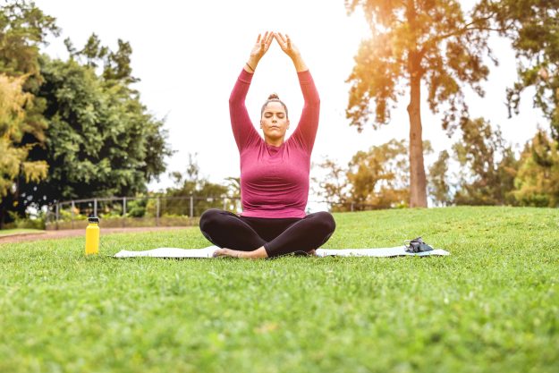 Curvy woman doing yoga meditation while keeping social distance