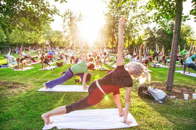 big group of adults attending a yoga class outside in park